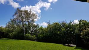 un campo verde con árboles y un cielo azul con nubes en Utesch's Ferienwohnungen, en Neuharlingersiel