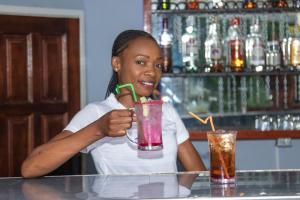 una mujer sentada en un bar sosteniendo una bebida en Elephant View Lodge & Apartments en Livingstone