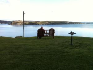 Un uomo seduto su una panchina che guarda l'acqua di The Bayside Bed and Breakfast a Bareneed