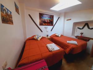 2 camas en una habitación con sábanas de color naranja en Hostal Raymi, en Ollantaytambo