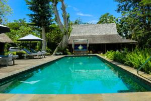 a swimming pool in front of a house with a thatch roof at Chanteak Bali in Jimbaran