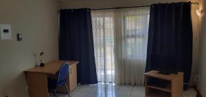 a room with a desk and a window with blue curtains at Liz' Cottage in Mbabane