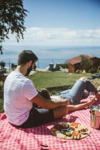 Ein Mann und eine Frau sitzen auf einer Picknickdecke mit einem Teller Essen. in der Unterkunft Madeira Sunset Cottage - Nature Retreat in Ponta do Pargo