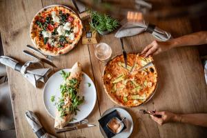 two pizzas on a wooden table with plates of food at Hotel Löwenhof in Bressanone