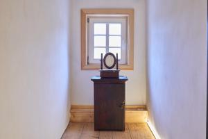 ein Zimmer mit einer Uhr auf einem Holzständer vor einem Fenster in der Unterkunft Doppelzimmer Anna Oberlausitzer Hof in Leutersdorf