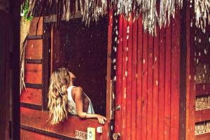 a woman sitting in front of a red door at Raiz Kite Cabana in Jericoacoara