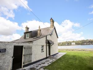 an old stone house with a gate and a body of water at Bwthyn Siliwen Old Bath House in Bangor