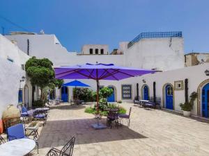 un patio con tavoli, sedie e ombrellone viola di Hôtel Bou Fares a Sidi Bou Saïd