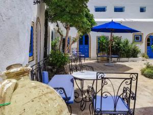 un patio con tavoli, sedie e ombrellone di Hôtel Bou Fares a Sidi Bou Saïd