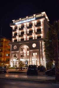 een verlicht gebouw met auto's voor het gebouw bij Hotel Lubjana in Durrës