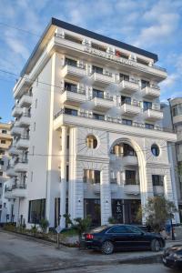 een groot wit gebouw met een auto ervoor geparkeerd bij Hotel Lubjana in Durrës