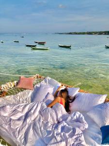 uma mulher deitada na cama debaixo de almofadas na praia em Indigo Blue Ceningan em Nusa Lembongan