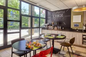 ein Restaurant mit 2 Tischen, Stühlen und Fenstern in der Unterkunft B&B HOTEL Saint-Quentin-en-Yvelines Centre Gare 4 étoiles in Montigny-le-Bretonneux