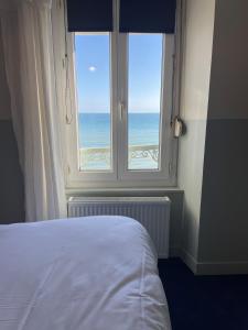 een slaapkamer met een raam met uitzicht op de oceaan bij Beau Rivage Hôtel-Restaurant in Luc-sur-Mer