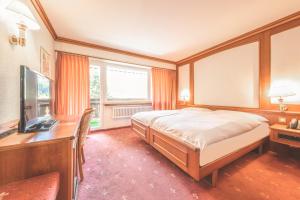 a bedroom with a bed and a desk and a television at Antares Hotel in Zermatt