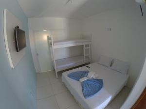 a small white room with a bed and a tv at Xodó do Peró Suítes in Cabo Frio