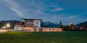 um edifício num campo com montanhas ao fundo em Ferienhotel Tyrol Söll am Wilden Kaiser em Söll