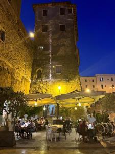 eine Gruppe von Personen, die vor einem Gebäude an Tischen sitzen in der Unterkunft Affittacamere Licenza N.1 Presso La Magica Torre in Pitigliano