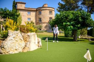 una mujer jugando al golf frente a un castillo en La Bastide De Tourtour Hotel & Spa, en Tourtour