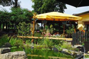 a garden with a yellow umbrella and a pond at Landhotel Heidekrug in Dohma