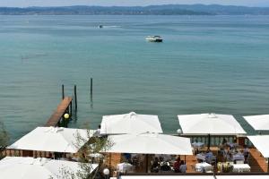 um restaurante com guarda-sóis brancos e um barco na água em Villa Pioppi Hotel em Sirmione