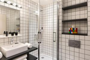 La salle de bains est pourvue de carrelage blanc, d'un lavabo et d'une douche. dans l'établissement RockyPop Grenoble Hotel, à Grenoble