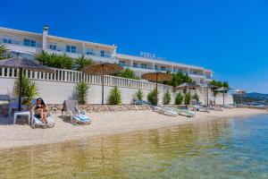 une femme assise sur une chaise sur la plage en face d'un hôtel dans l'établissement Hotel Perla, à Rogoznica