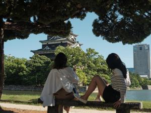 deux femmes assises sur un banc devant une tour dans l'établissement fav HIROSHIMA STADIUM, à Hiroshima