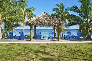 a group of blue chairs and a straw umbrella on the beach at Sunset Resort in Rarotonga