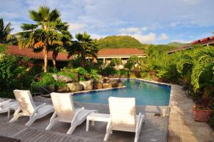 a swimming pool with white chairs and a house at Sunset Resort in Rarotonga