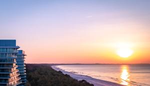 Blick auf ein Gebäude und den Strand bei Sonnenuntergang in der Unterkunft Wave Międzyzdroje Resort & SPA in Misdroy