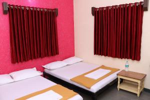 duas camas num quarto com cortinas vermelhas e uma mesa em Hotel laxminarayan em Shirdi