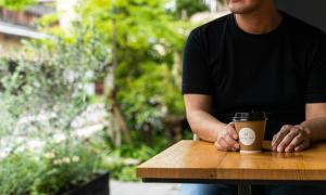 Un uomo seduto a un tavolo con una tazza di caffè di HOTEL RINGS KYOTO a Kyoto