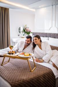 a man and woman laying on a bed with a tray of food at Amsterdam Hotel in Belgrade