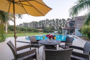 a patio with a table and chairs and an umbrella at StayVista at The Banyan Abode with Pool Table, Pet Friendly & Outdoor Pool in Manesar