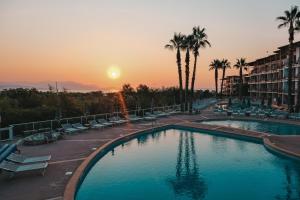 een groot zwembad met stoelen en palmbomen bij zonsondergang bij Thalazur Antibes - Hôtel & Spa in Antibes