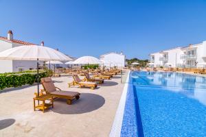 een rij stoelen en parasols naast een zwembad bij Naranjos Resort Menorca in S'Algar