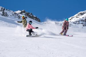 Tre persone stanno facendo snowboard su una pista innevata di Peaks Place Apartments & SPA a Laax