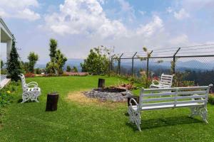 zwei weiße Bänke auf einem Hof mit Feuerstelle in der Unterkunft StayVista at The Lilly Ooty with Breakfast in Udagamandalam