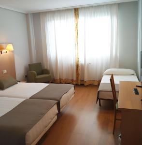 a hotel room with two beds and a desk and a window at Hotel San Millán in Santander