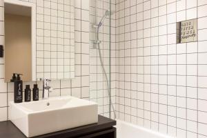 La salle de bains est pourvue de carrelage blanc, d'un lavabo et d'une douche. dans l'établissement RockyPop Grenoble Hotel, à Grenoble