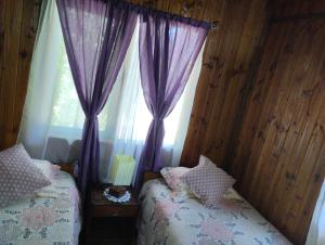 a bedroom with two beds and a window with purple curtains at Hospedaje Picoyo in Pucón