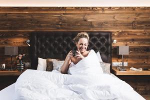 Eine Frau, die im Bett liegt und ihr Handy ansieht. in der Unterkunft Alpines Gourmet Hotel Montanara in Flachau