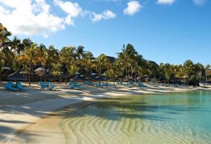 a beach with chairs and palm trees and the water at Royal Palm Beachcomber Luxury in Grand Baie