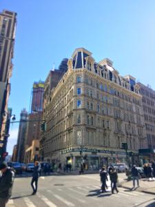 - un grand bâtiment dans une rue de la ville où les gens traversent la rue dans l'établissement NYC Empire Apartments, à New York