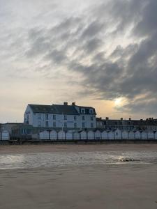 een wit gebouw op het strand met een bewolkte hemel bij Beau Rivage Hôtel-Restaurant in Luc-sur-Mer