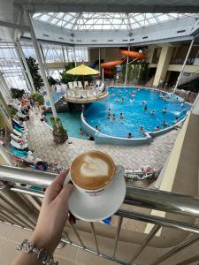 une personne tenant une tasse de café en face d'une piscine dans l'établissement Hotel Alinalex - Paradisul Acvatic, à Braşov