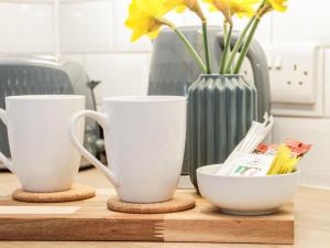 two white cups sitting on a cutting board with a vase at Tŷ Capel Bach in Bangor