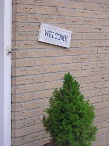 a welcome sign on a brick wall with a tree at Rose Cottage B&B in Nes