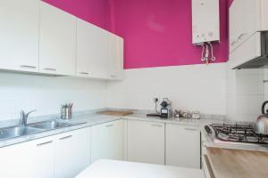 una cucina con armadietti bianchi e parete rosa di Brera Apartments in San Marco a Milano